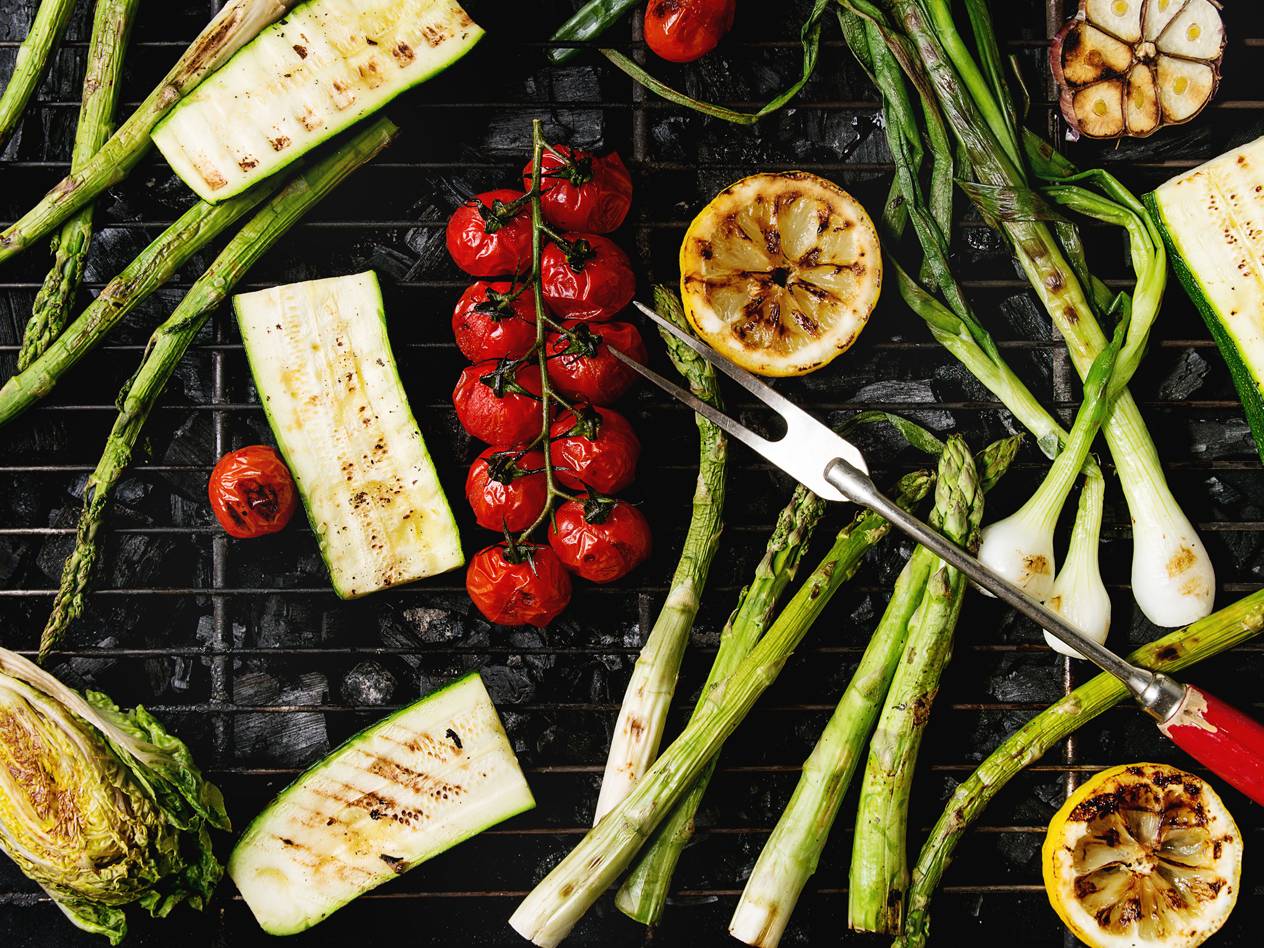 Gegrilltes Gemüse wie Zucchini, Spargel, Tomaten, Zitronen und Frühlingszwiebeln auf einem Grillrost.