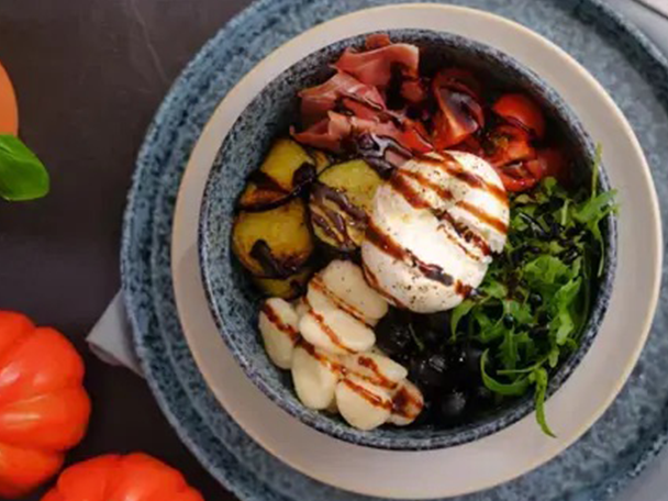 Bunte Schüssel mit Mozzarella, Prosciutto, gegrilltem Gemüse, Tomaten und Rucola.