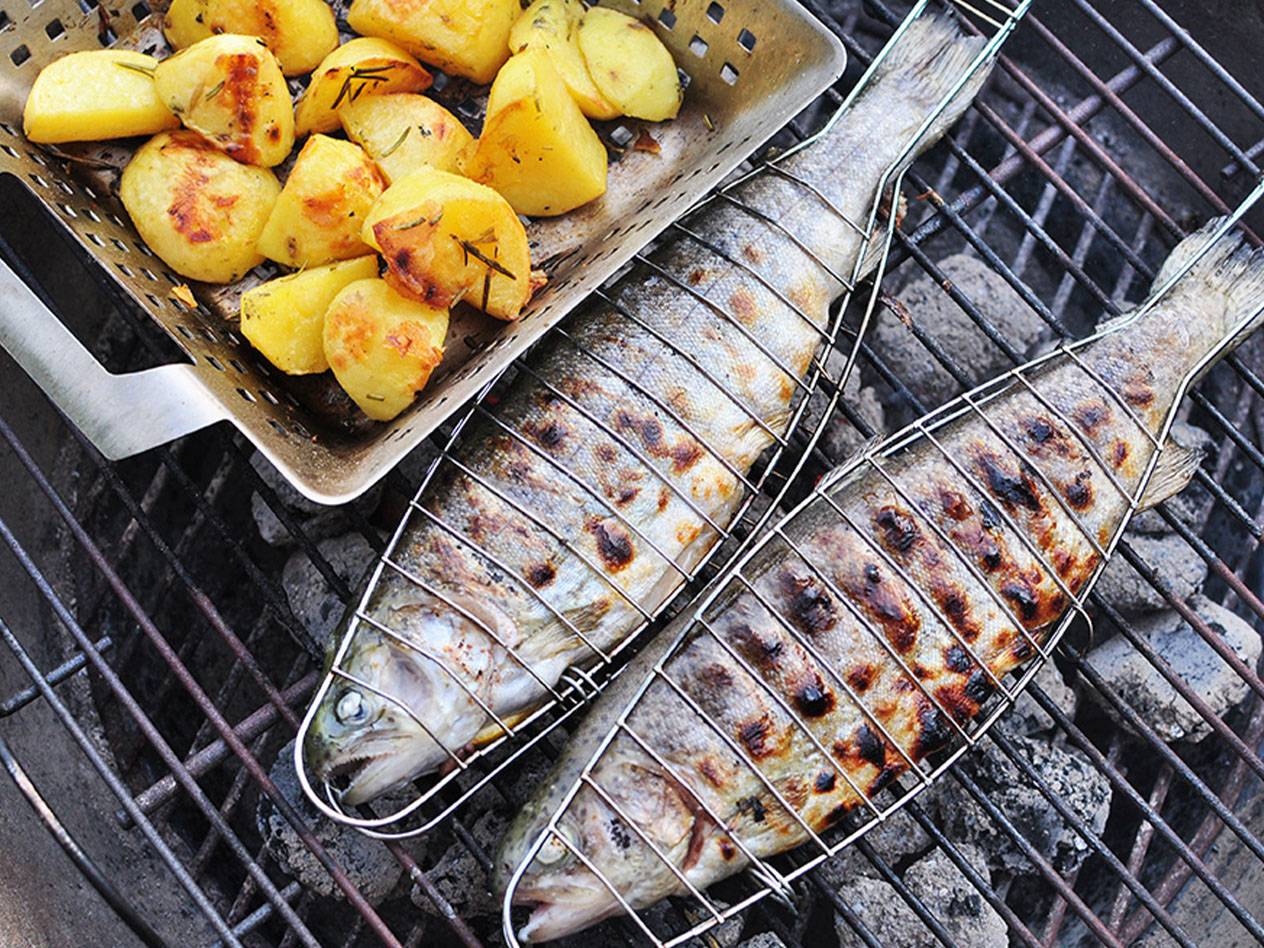 Zwei gegrillte Fische und Kartoffeln auf einem Grillrost.