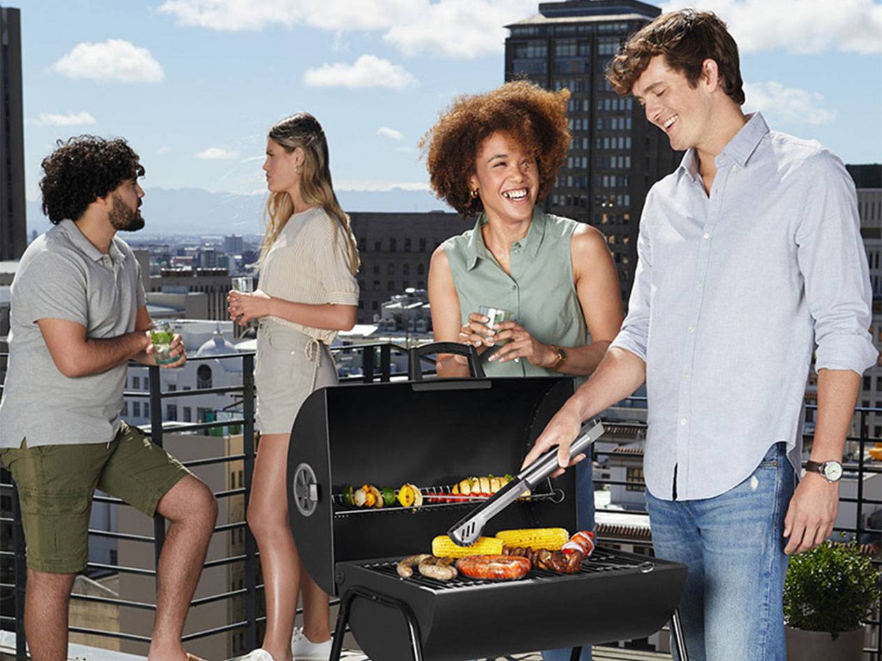 Vier Freunde grillen auf einer Dachterrasse mit Blick auf die Stadt.