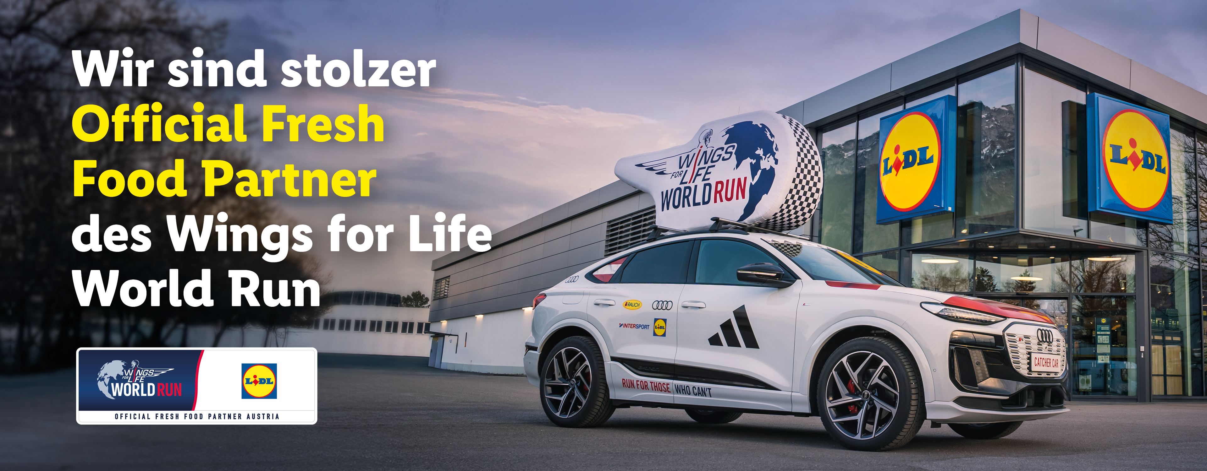 Ein weißes Auto mit einem großen Pfeifen-Dachaufsatz steht vor einem Supermarkt, der als offizieller Frischepartner des Wings for Life World Run beworben wird.