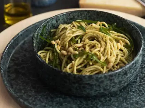 Spaghetti mit Pesto, Rucola und Pinienkernen in einer dunklen Schale