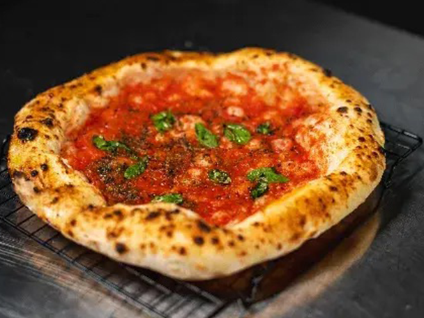 Eine frisch gebackene Pizza Margherita mit Basilikumblättern auf einem Rost.