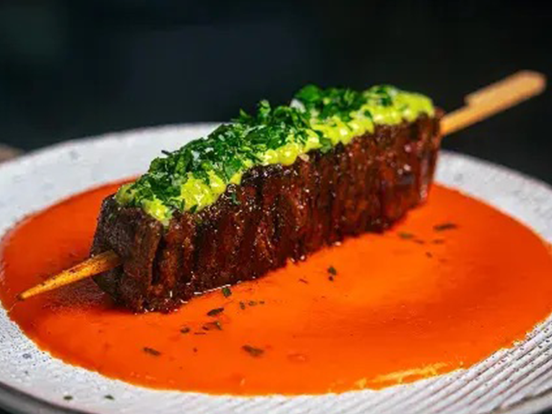 Fleischspieß mit grüner Kräutersauce auf rotem Spiegel