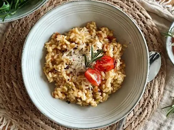 Cremiges Risotto mit Kirschtomaten, Rosmarin und geriebenem Käse in einer Schüssel auf einem Stroh-Tischset.