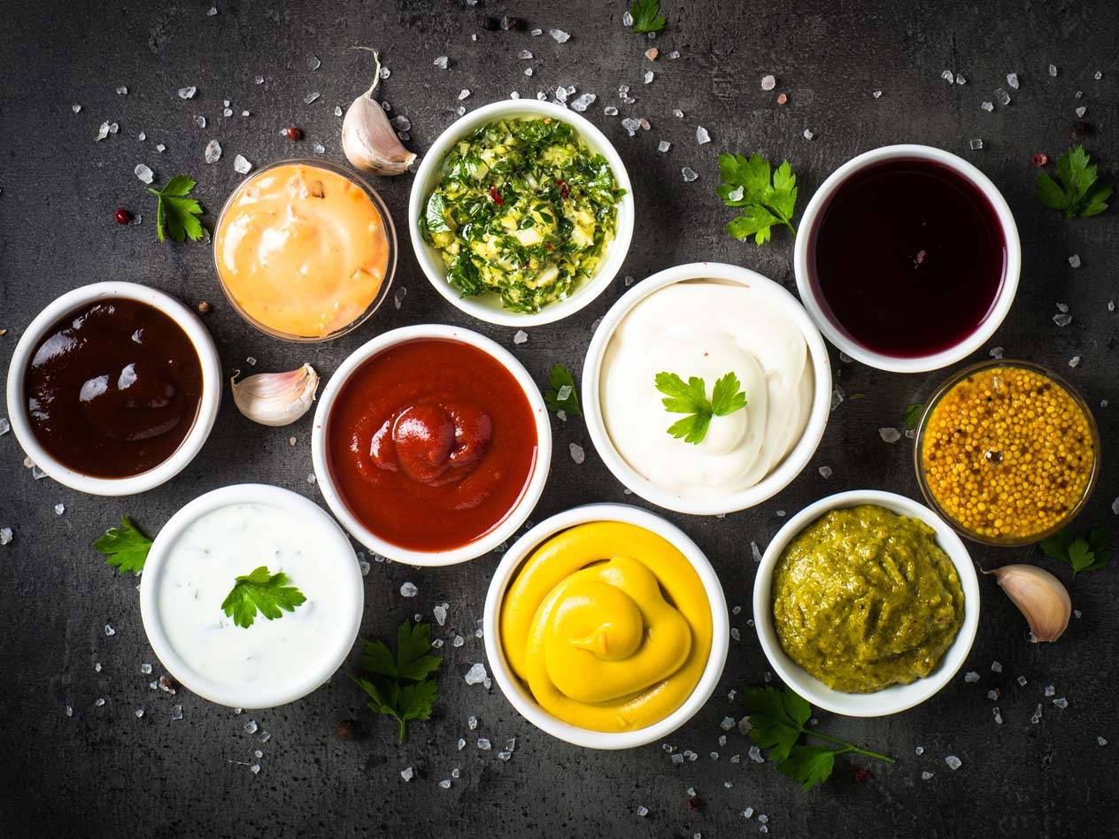 Eine Auswahl an Saucen und Dips in kleinen Schalen, darunter Ketchup, Senf, Mayonnaise und Barbecue-Sauce.