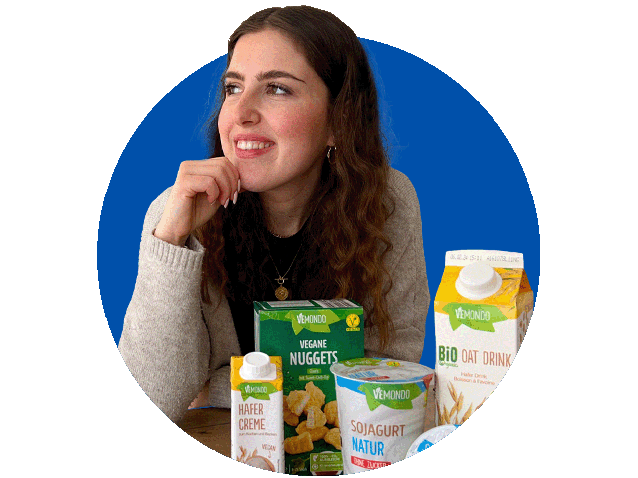Eine Frau lächelt neben Vemondo Hafercreme, veganen Nuggets, Sojajoghurt Natur und Bio Haferdrink.