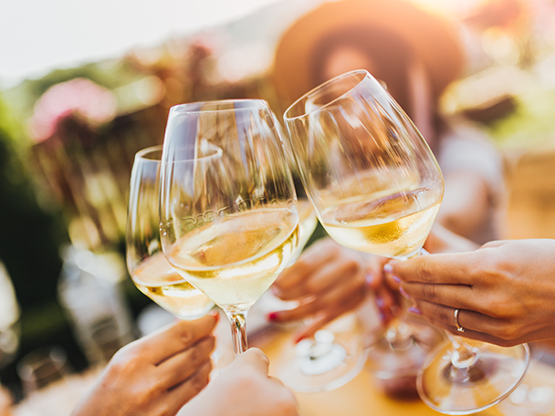 Gruppe von Freunden stößt mit Weißweingläsern im Freien an.