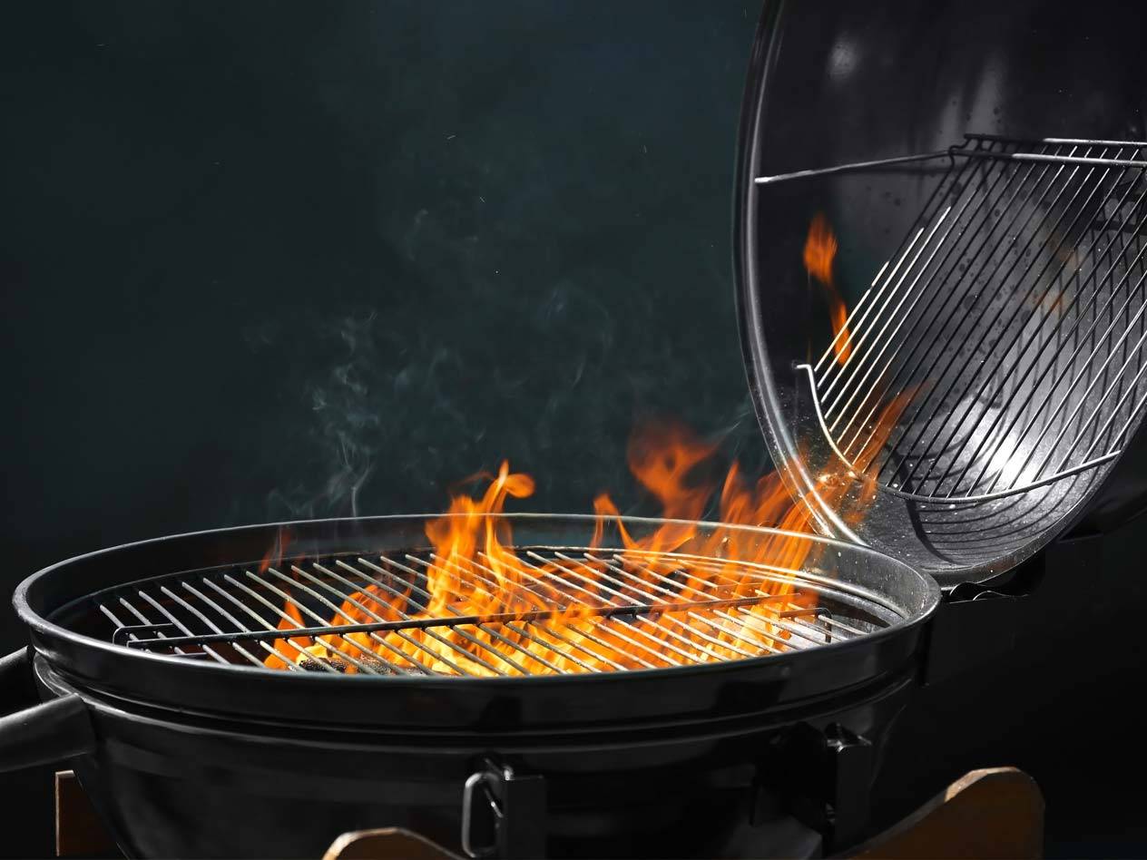 Ein schwarzer Grill mit lodernden Flammen und Rauch, der aus dem Rost aufsteigt.