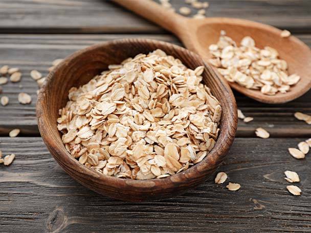 Haferflocken in einer Holzschale und auf einem Holzlöffel auf einem Holztisch.