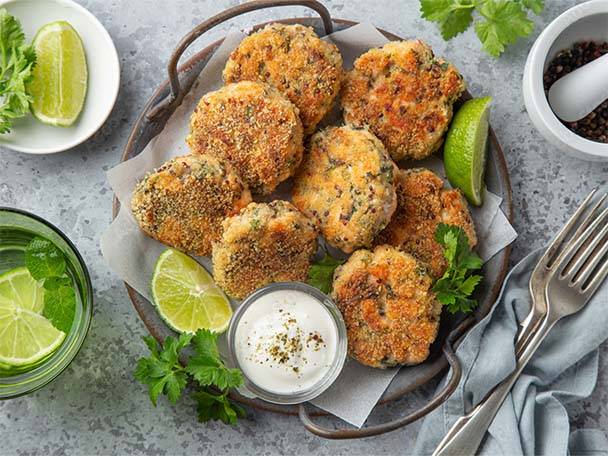 Eine Platte mit goldbraunen Fischfrikadellen, Limettenspalten und einer Schale Dip.