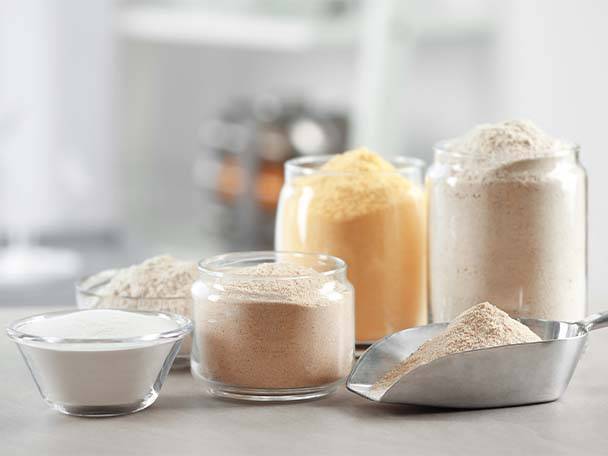 Verschiedene Mehlsorten in Gläsern und Schalen auf einer Arbeitsplatte.