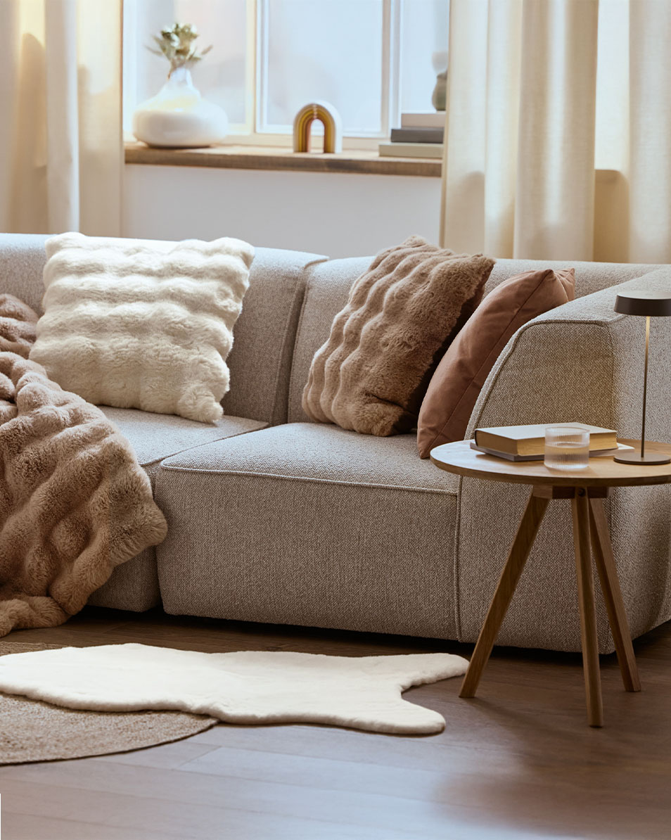 Graues Modulsofa mit flauschigen Kissen und Decken, Beistelltisch aus Holz.