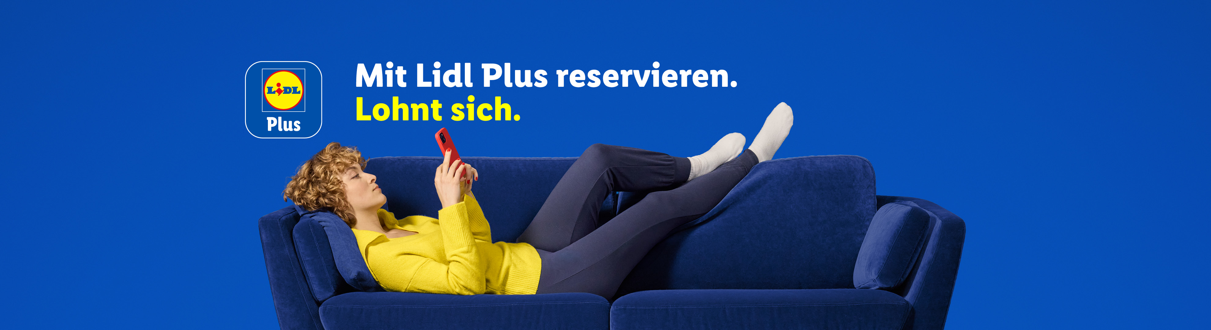 Eine Frau liegt auf einem blauen Sofa und schaut auf ihr Smartphone. Text: Mit Lidl Plus reservieren. Lohnt sich.