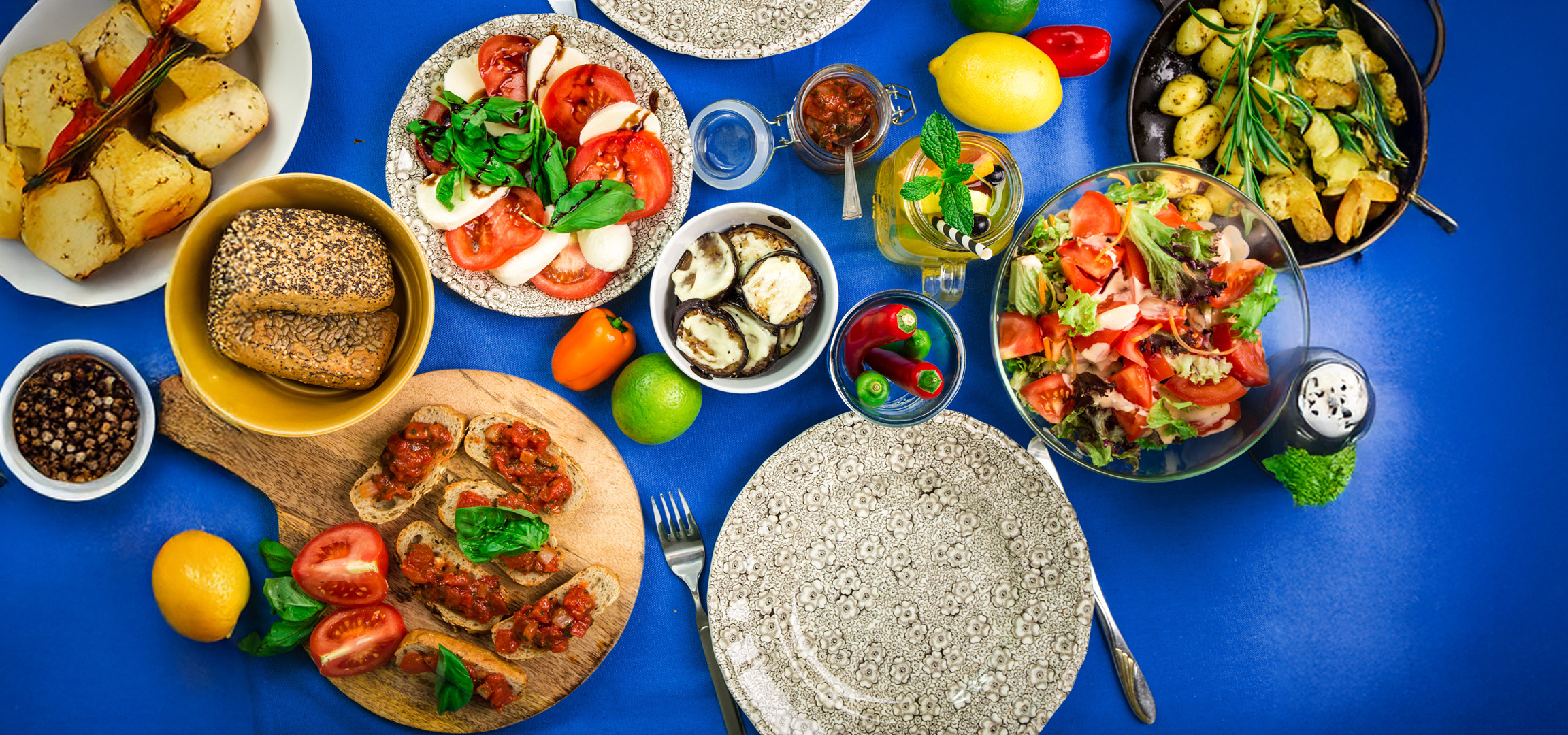 Brot, Bruschetta, Salat und gegrillte Auberginen auf blauem Hintergrund.